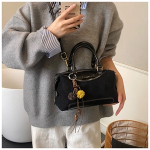 Detail of black textured crossbody bag with plush pom-poms and long tassels accent
