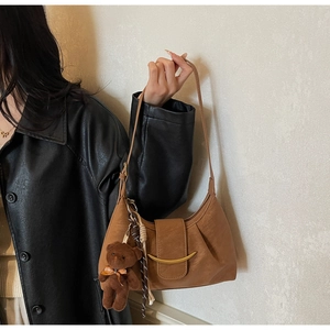 Detail of a brown leather underarm bag with gold metal trim and a cute teddy bear charm