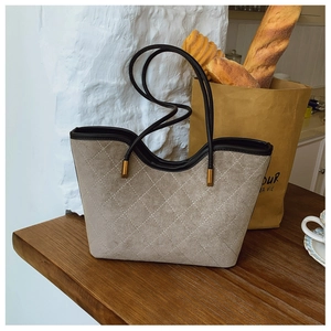 Detail of quilted suede tote bag with black leather handles and gold metal accents