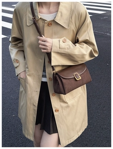 Close-up of brown vintage crossbody bag styled with a khaki trench coat outdoors