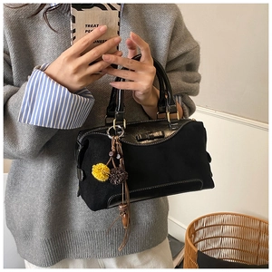 Detail of black suede handbag featuring a matching bow and decorative pom-pom bag charm