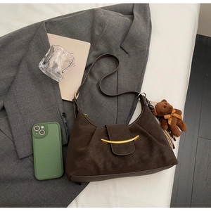Brown moon shoulder bag with gold clasp and plush bear charm on minimalist background