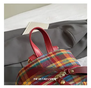 Detailed close-up of vibrant plaid backpack fabric with red leather handle and gold zippers
