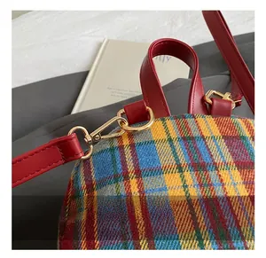 Detailed close-up of high-quality golden metal hooks and red leather straps on plaid bag