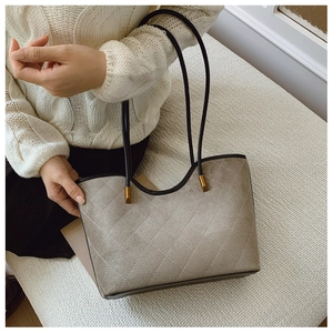 Detail of grey quilted suede tote bag with black leather straps and gold metal accents