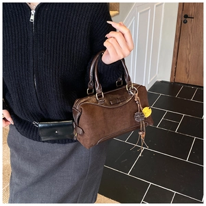 Detail of dark brown suede shoulder bag with decorative bow and colorful pompom charms