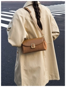 Brown leather crossbody bag shown on a model in a stylish street style trench coat