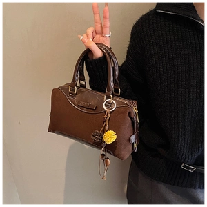Detailed close-up of dark brown Boston bag with fuzzy pom-pom charm and golden hardware