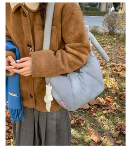 Detail of grey puffer tote bag with Fashion tag worn by model in outdoor setting