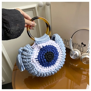 Détail du sac tricoté avec motif œil bleu et poignées rondes en résine ambrée