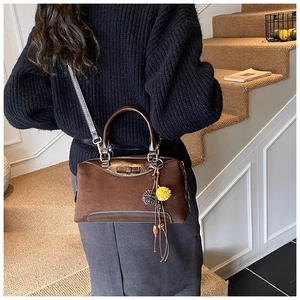 Detail of dark brown suede doctor bag with leather handles and decorative pompom charm