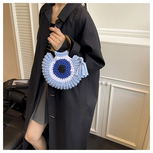 Détail du sac bohème en tricot avec poignées en résine et pompons bleus