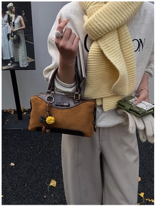 Detail of a brown suede Boston bag with colorful pom-pom charms in an autumn street setting