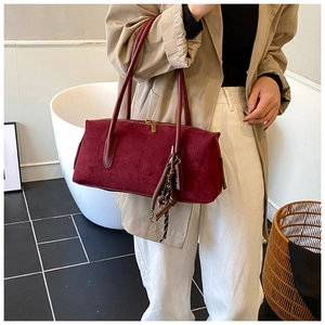 Détail du sac Boston en daim bordeaux avec doubles poignées et pendentif à glands