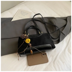 Detail of black crossbody bag with bow accent and fur pompom charm next to a phone