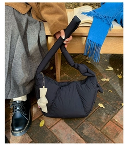 Detail of a black quilted nylon crossbody bag featuring a soft knot charm on a wooden bench