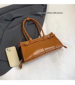 Brown leather shoulder bag shown with a smartphone for size reference and scale
