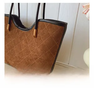 Detail of brown suede tote bag with diamond stitching, black handles and gold hardware