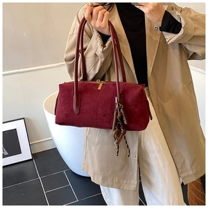 Détail d'un sac Boston en daim bordeaux avec de longues anses et un charme rétro en bois