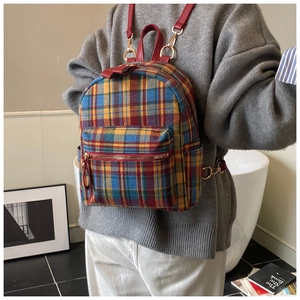 Dettaglio degli spallacci in pelle rossa e motivo tartan su uno zaino invernale chic