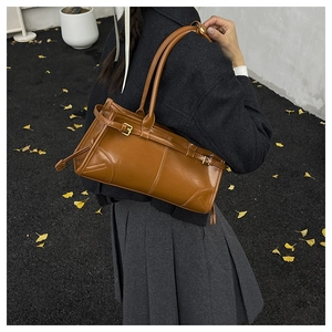 Detail of vintage brown leather baguette bag worn over the shoulder against ginkgo leaves