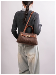 Detail view of brown woven handbag with gold X-buckle strap on a casual model