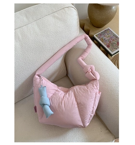 Detail of pink quilted puffer bag with a blue knot charm on a white armchair