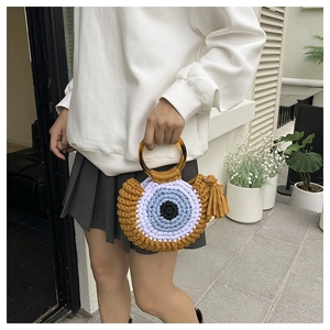 Détail du sac tricoté main en coton avec motif œil et poignées rondes en résine