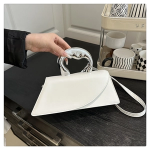 Detail of white geometric handbag with sculptural silver metal handle on a wooden table