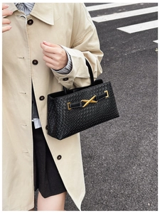 Close-up of a black woven leather tote bag featuring a gold X-shaped metal buckle detail