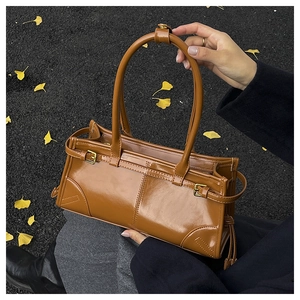 Detail of caramel glossy leather handbag with buckle strap against autumn leaves