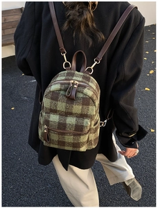 Detailed outdoor shot of green and brown plaid wool backpack with leather straps and gold zippers