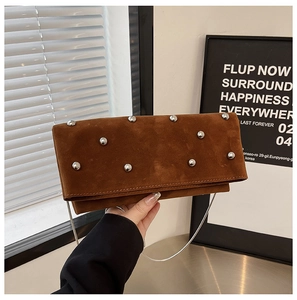 Brown suede shoulder bag with silver studs and chain strap held against a minimalist wall