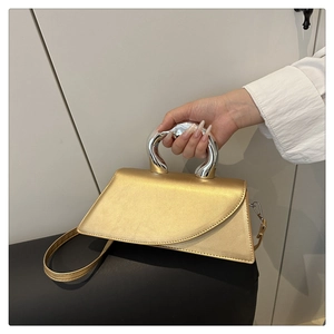 Detail of the golden crossbody bag with an irregular silver metal handle and asymmetric flap
