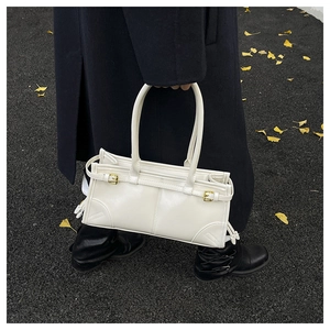 Close-up of a white leather tote bag with buckle detail held by a model in winter coat