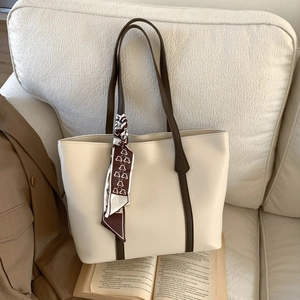 Chic cream leather tote bag with brown straps and silk scarf detail on a soft sofa