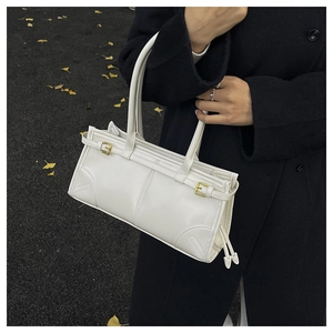 Close-up of white leather handbag with golden buckle and tassel details on a street