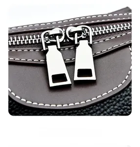 Detail of contrast stitching and dual metal zippers on a bi-color leather pillow bag