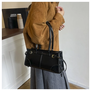 Side view of black glossy patent leather shoulder bag with gold buckles on model