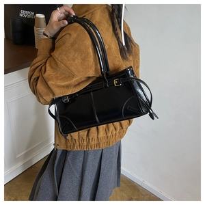 Detail of a vintage black glossy shoulder bag with gold buckle on a model's shoulder
