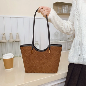 Brown quilted tote bag with black straps and gold accents for women in a cafe setting