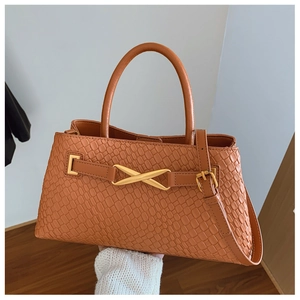 Detail of woven texture on tan handbag with gold X-shaped metal buckle and top handle