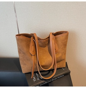 Macro detail of brown suede tote bag with leather piping on a black book prop