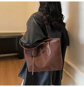 Detail view of a large dark brown suede tote bag worn over the shoulder by a model