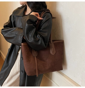 Detail of deep brown suede tote bag with slim shoulder strap shown on model in leather jacket