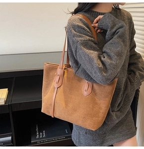 Close-up of brown suede tote bag with leather strap on a model in a library