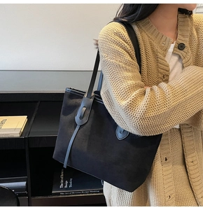 Close-up of a black suede-textured tote bag showing soft material and strap details