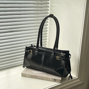Minimalist black glossy leather underarm bag with gold hardware on a decorative book
