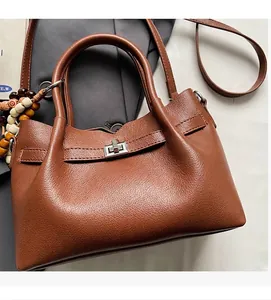 Détail d'un sac en cuir marron à motif litchi avec fermoir rotatif argenté et breloque