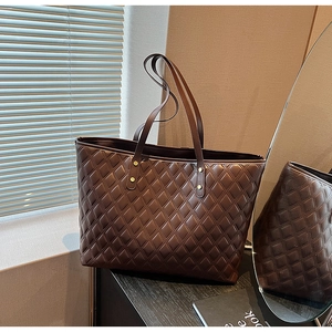 Dettaglio borsa shopper trapuntata marrone scuro con rivetti dorati su tavolo in legno